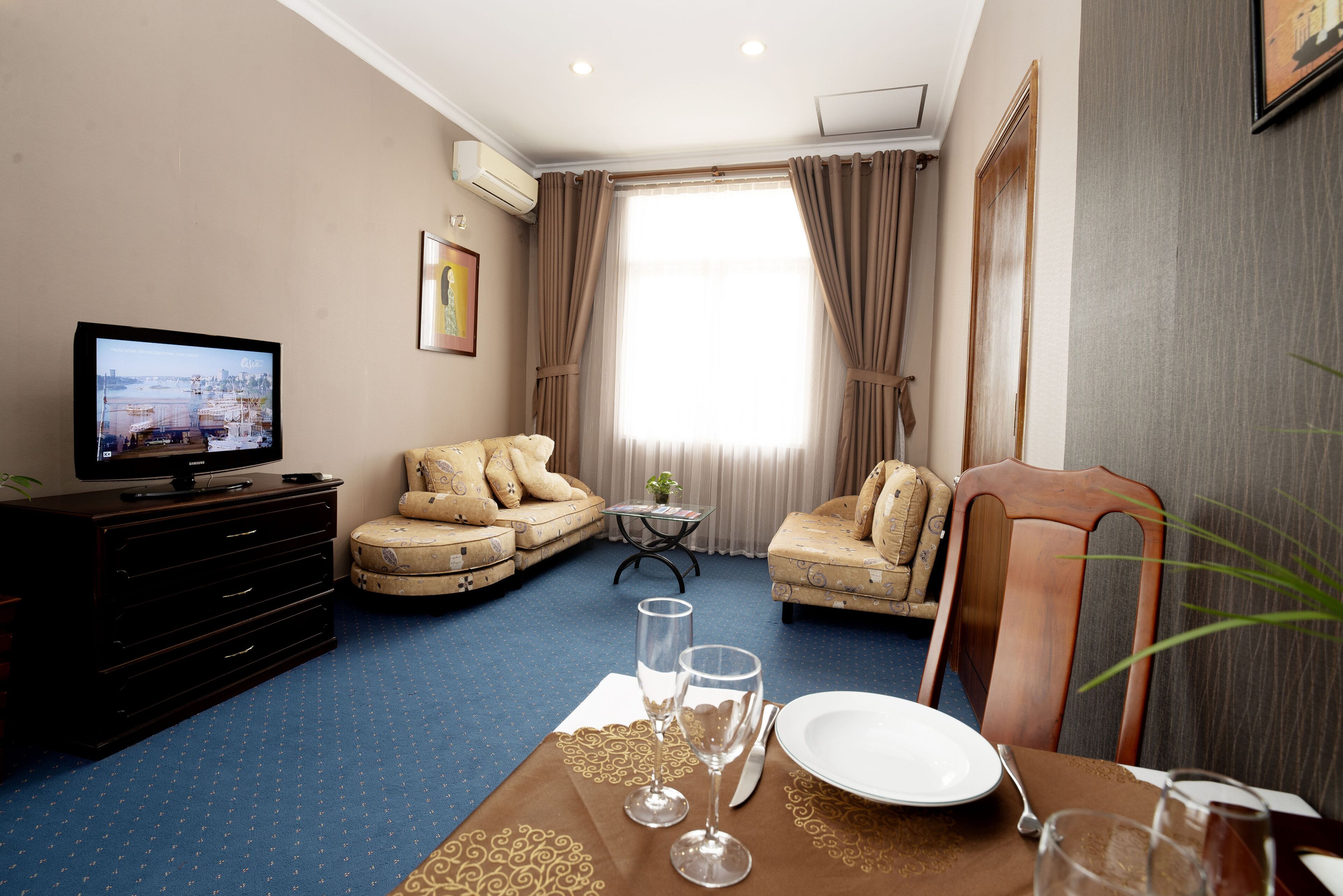 Une chambre d’hôtel équipée d’une télévision, de deux canapés, d’une table à manger dressée avec une assiette, des verres et des couverts.