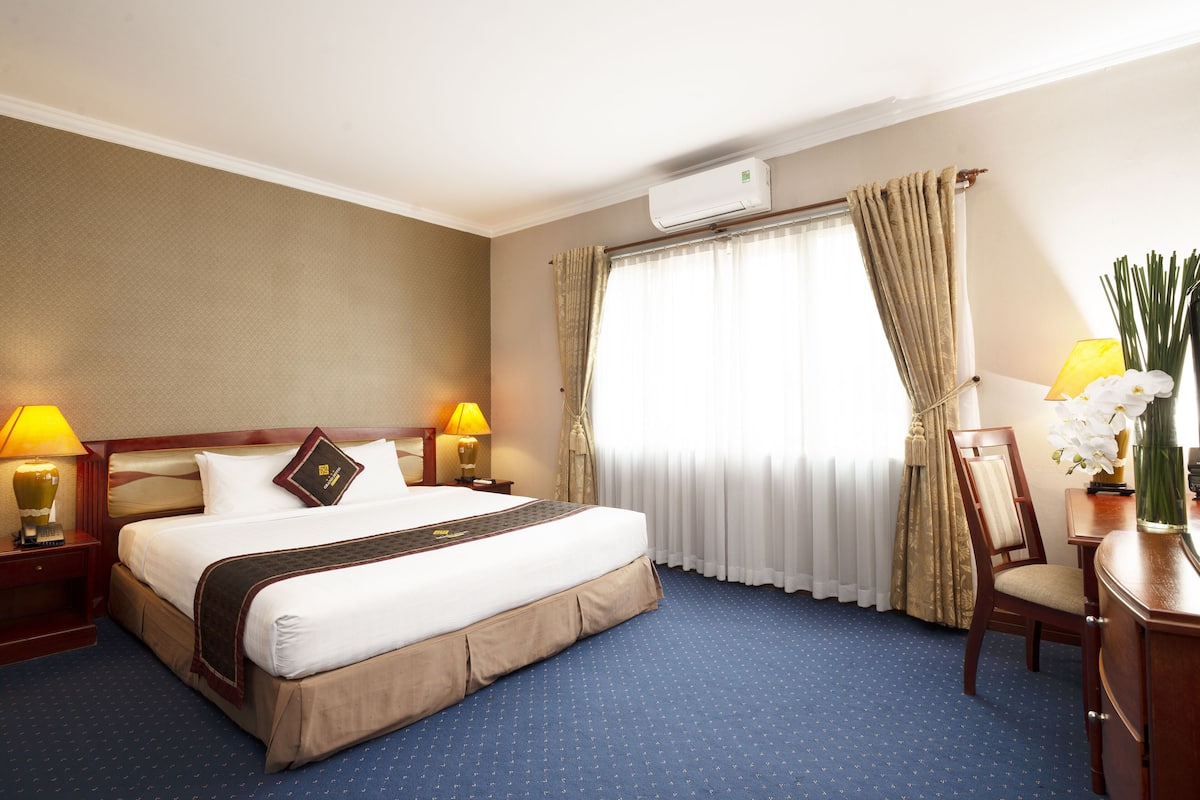 Una habitación de hotel con una cama grande, dos mesitas de noche con lámparas, una silla, un escritorio y una ventana con cortinas.