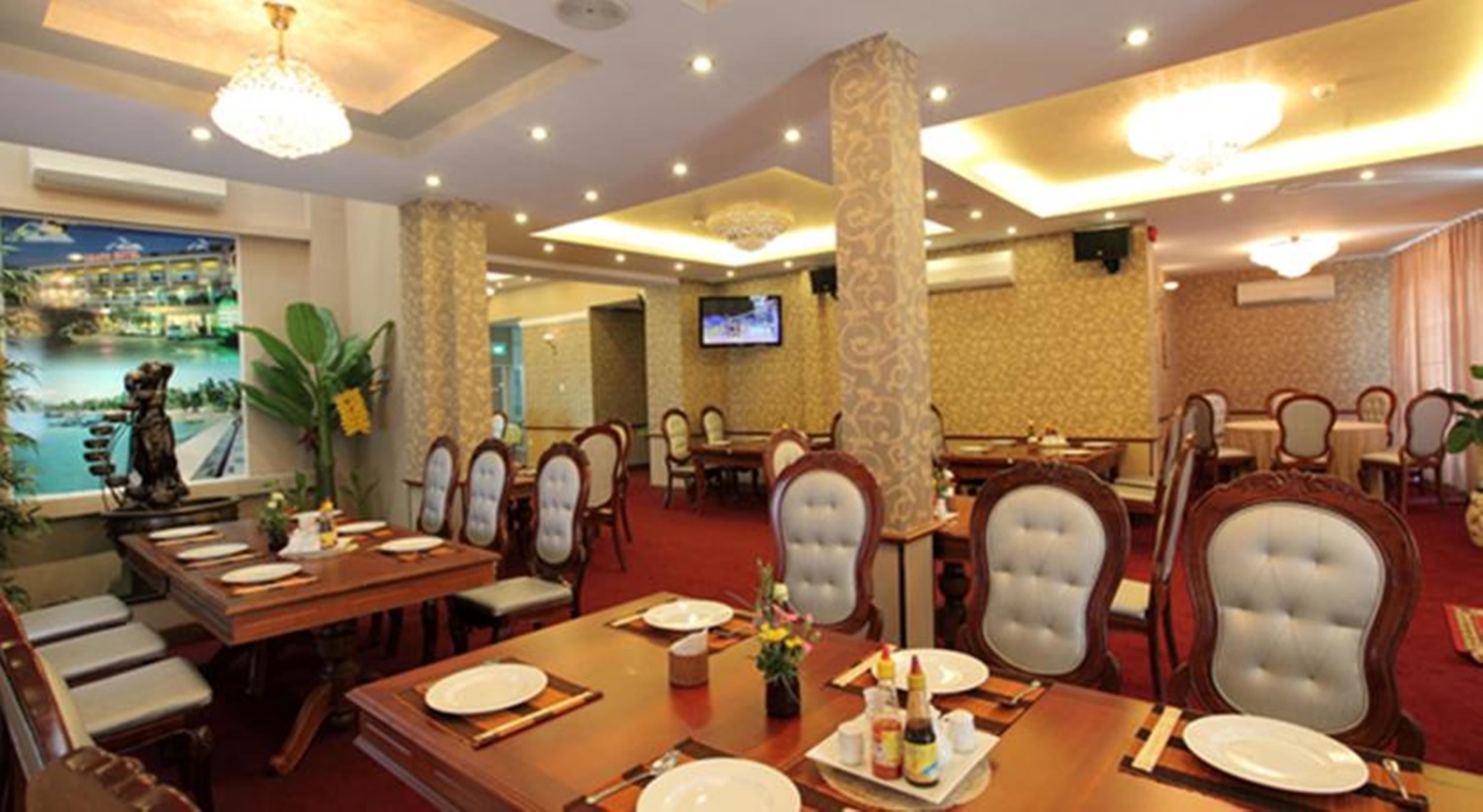 Une salle à manger d’hôtel avec plusieurs tables et chaises, un téléviseur fixé au mur et une vue panoramique sur la côte, visible par une fenêtre.