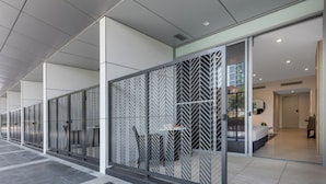 A modern hotel corridor with patterned glass partitions, a tiled floor, and a glimpse of a bedroom with a bed and a desk.