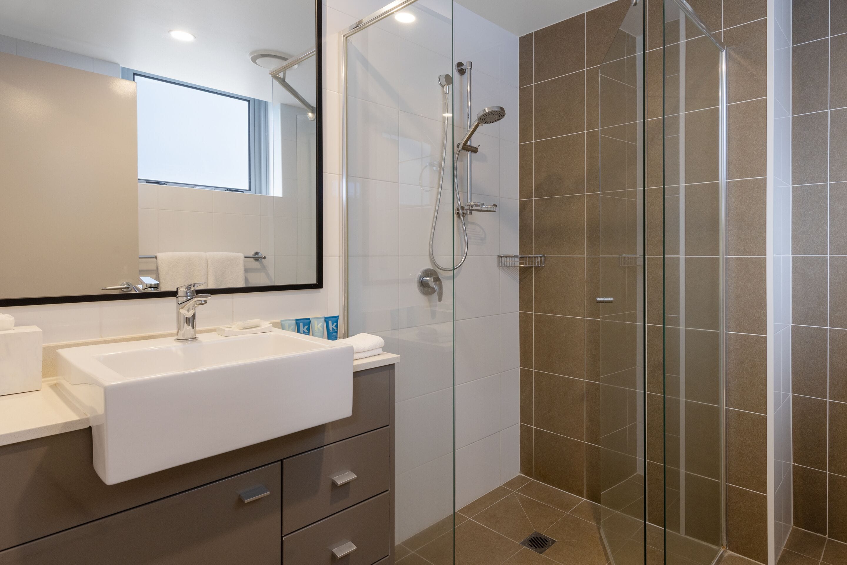 A modern bathroom with a white sink, mirror, and glass shower enclosure.