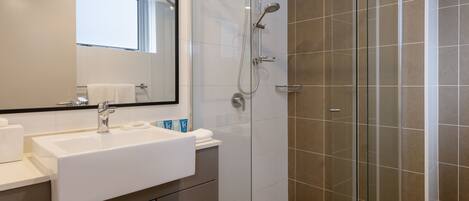 A modern bathroom with a white sink, mirror, and glass shower enclosure.