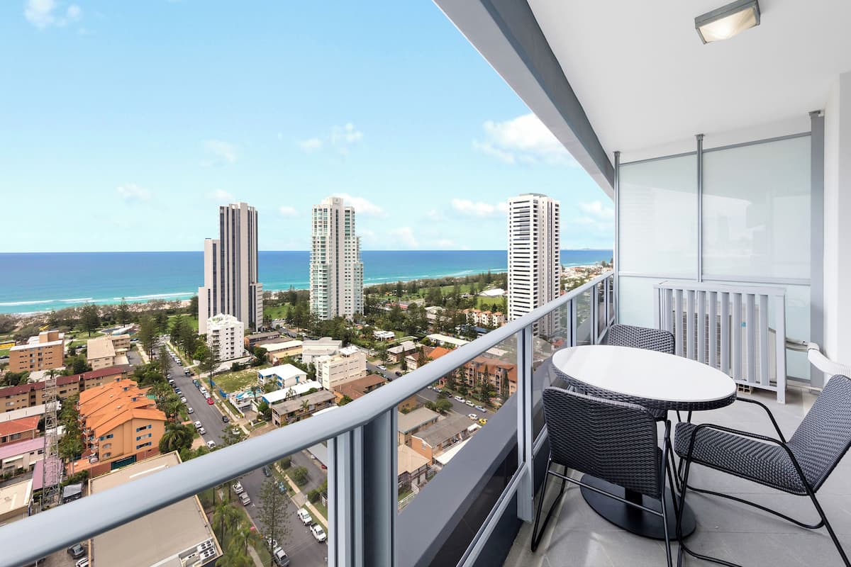 A balcony with a table and chairs overlooking a cityscape and beach.