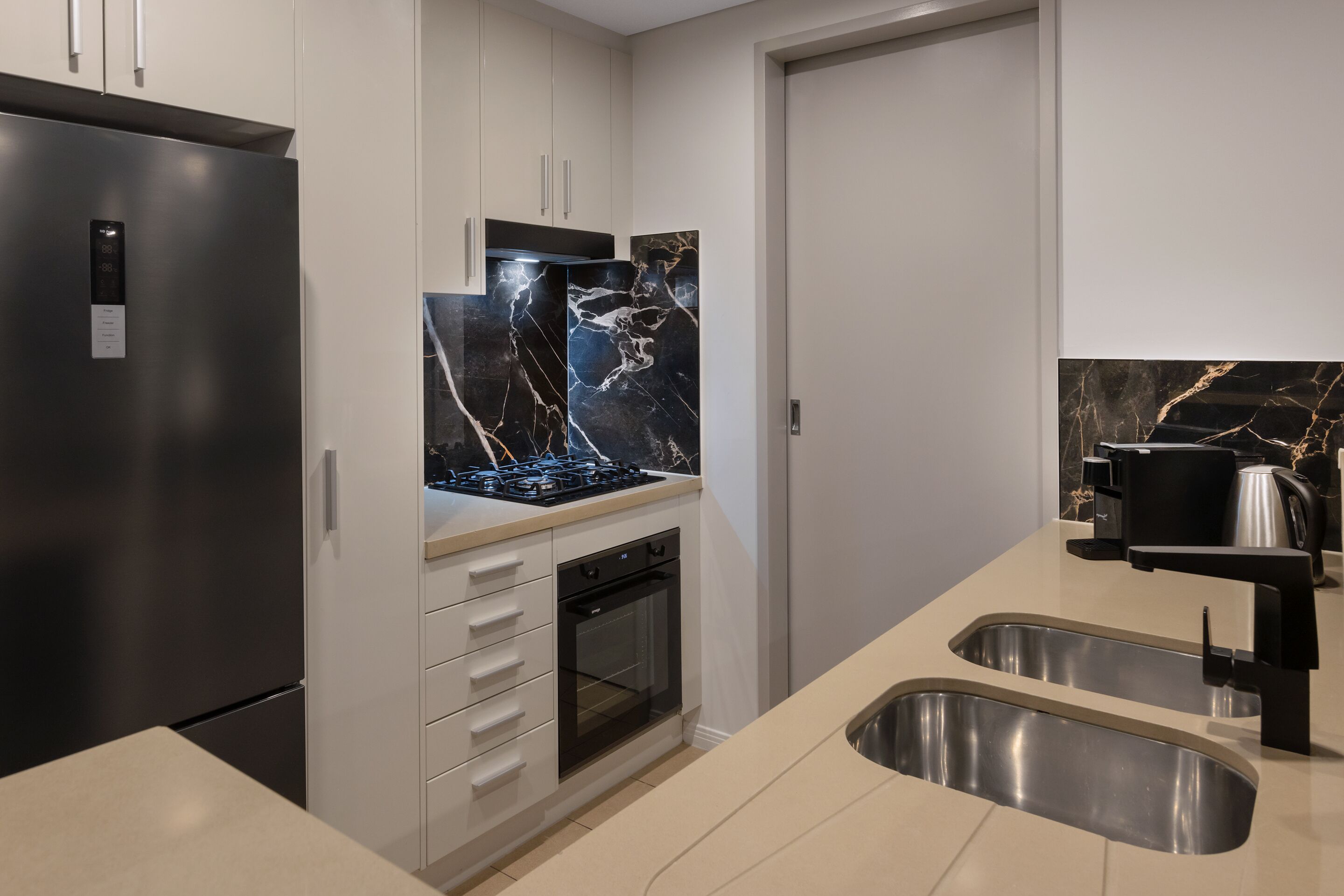 Una cucina moderna con frigorifero in acciaio inossidabile, forno integrato, lavello a due vasche e pannello di copertura in marmo.