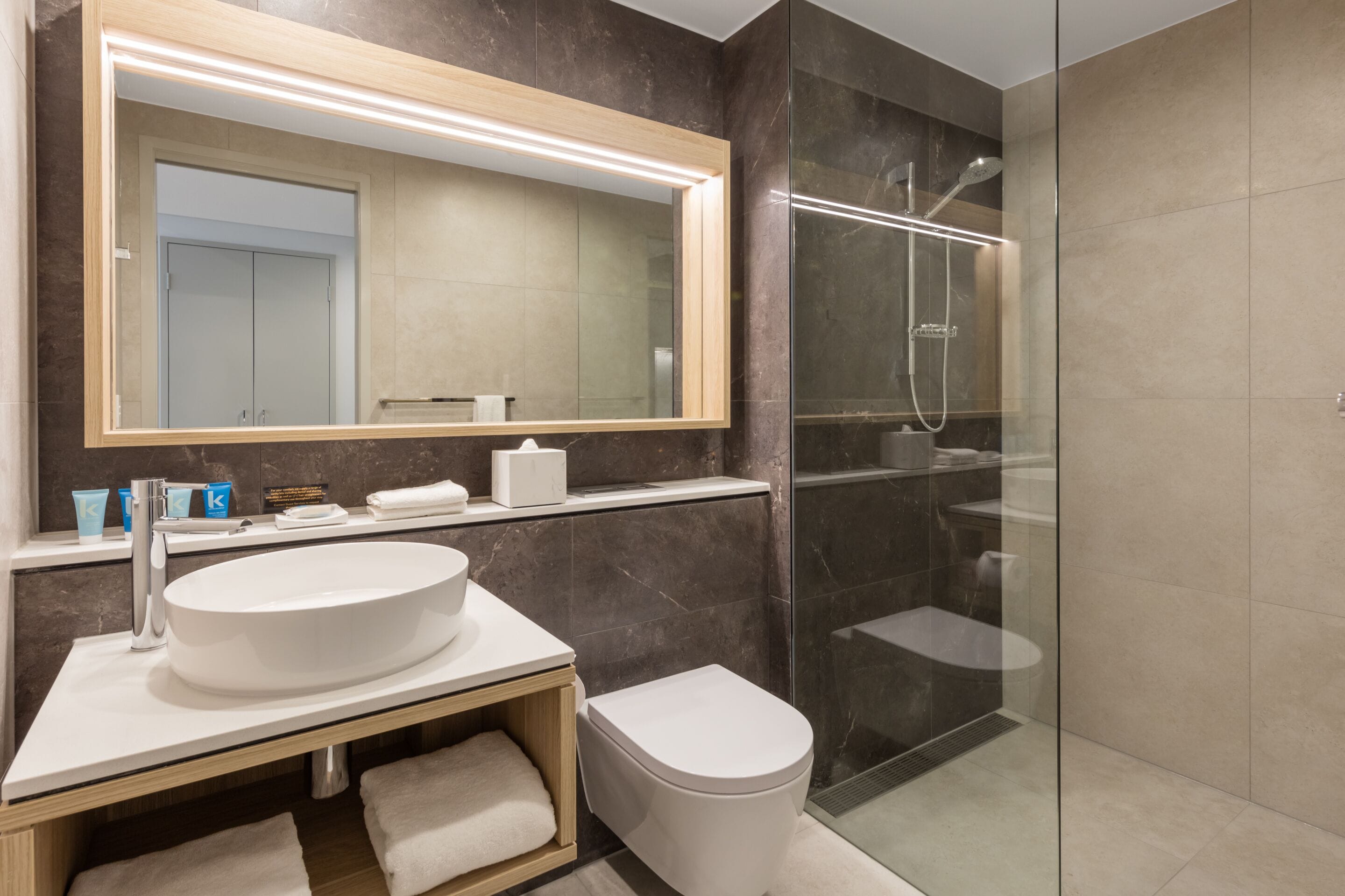 A modern bathroom with a large mirror, a sink, a toilet, and a glass-enclosed shower area.