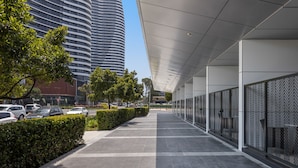 A modern building with a curved facade, a covered walkway, and a parking area with cars.
