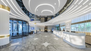 A modern hotel lobby with a marble floor, curved reception desk, and a large window offering a view of the outdoors.