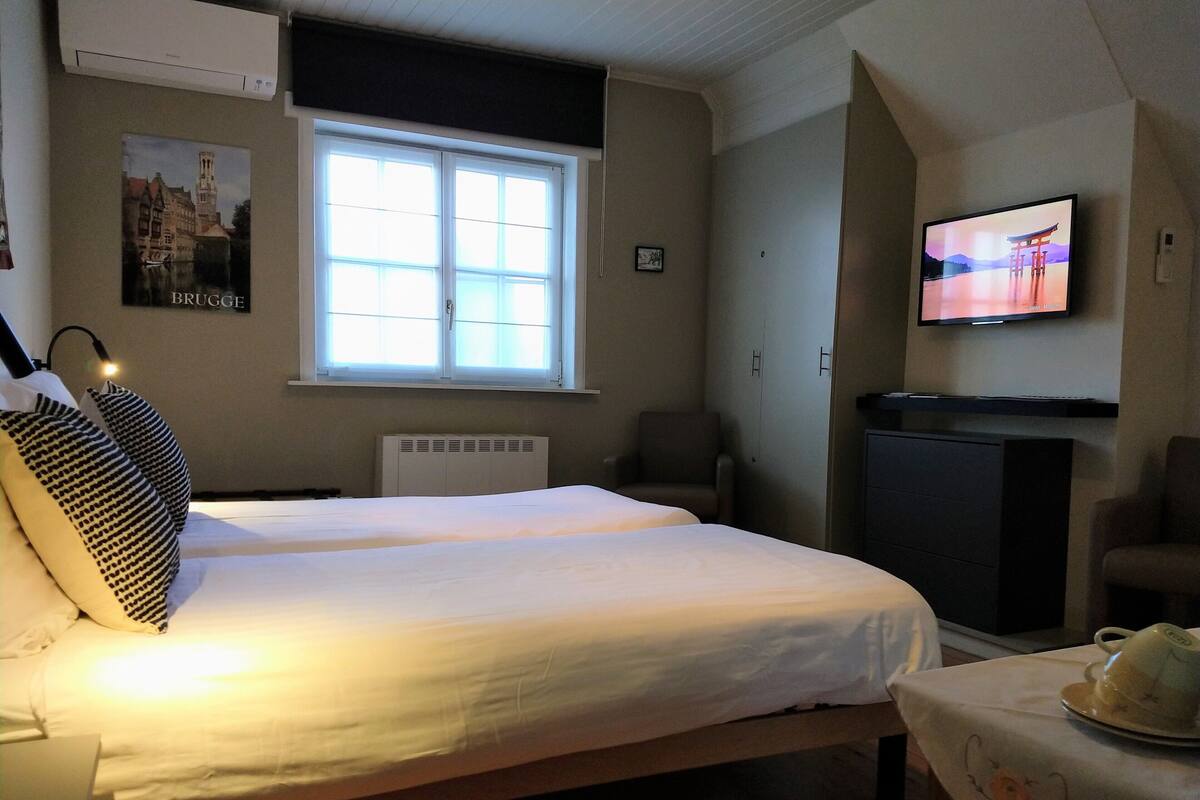A hotel room with two beds, a television, a radiator, and a window with blinds.