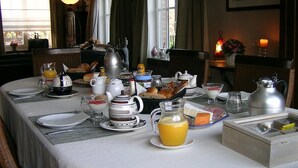Una mesa de desayuno dispuesta con diversos platos, incluyendo una jarra de jugo de naranja, una tetera y una variedad de pasteles y pan.