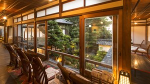 Une pièce de style japonais traditionnel, avec des tatamis, des meubles en bois et de grandes fenêtres donnant sur un jardin et des bâtiments traditionnels.