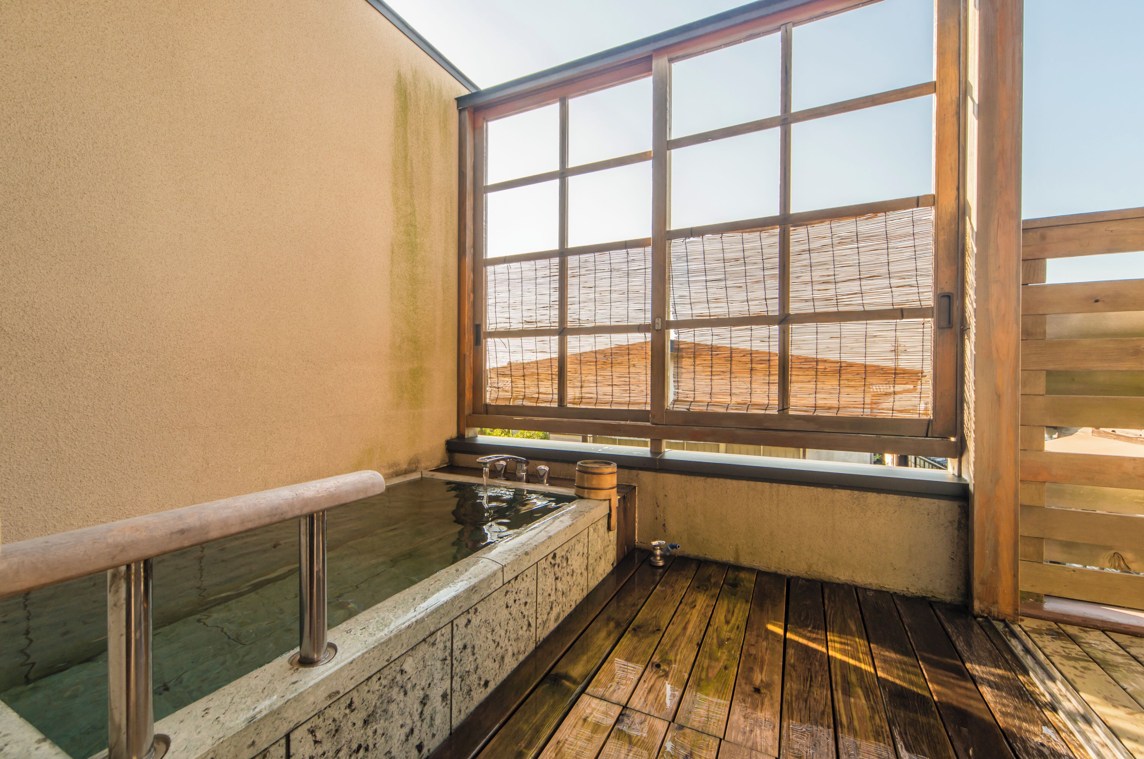 Een traditionele Japanse onsen met een houten terras, een stenen warmwaterbron en uitzicht op een berglandschap door een groot raam.