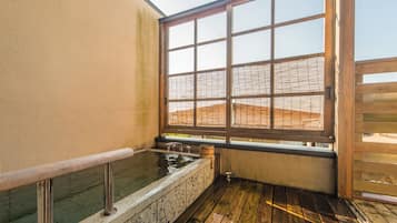Een traditionele Japanse onsen met een houten terras, een stenen warmwaterbron en uitzicht op een berglandschap door een groot raam.