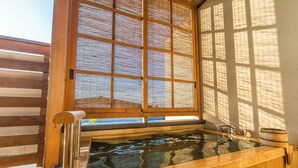 Un bain à remous en bois doté d’une fenêtre au-dessus, permettant à la lumière du soleil de pénétrer.