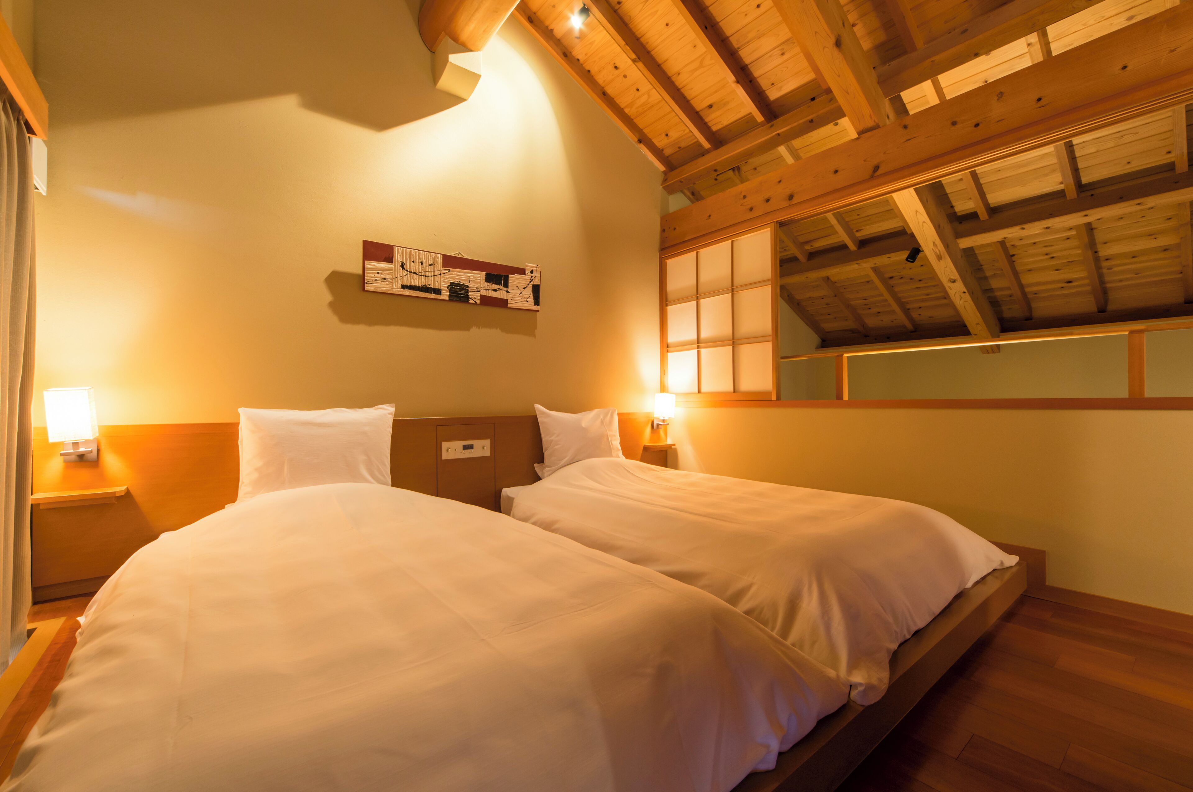 A hotel room with two beds, wooden ceiling beams, a wall-mounted artwork, and bedside lamps.