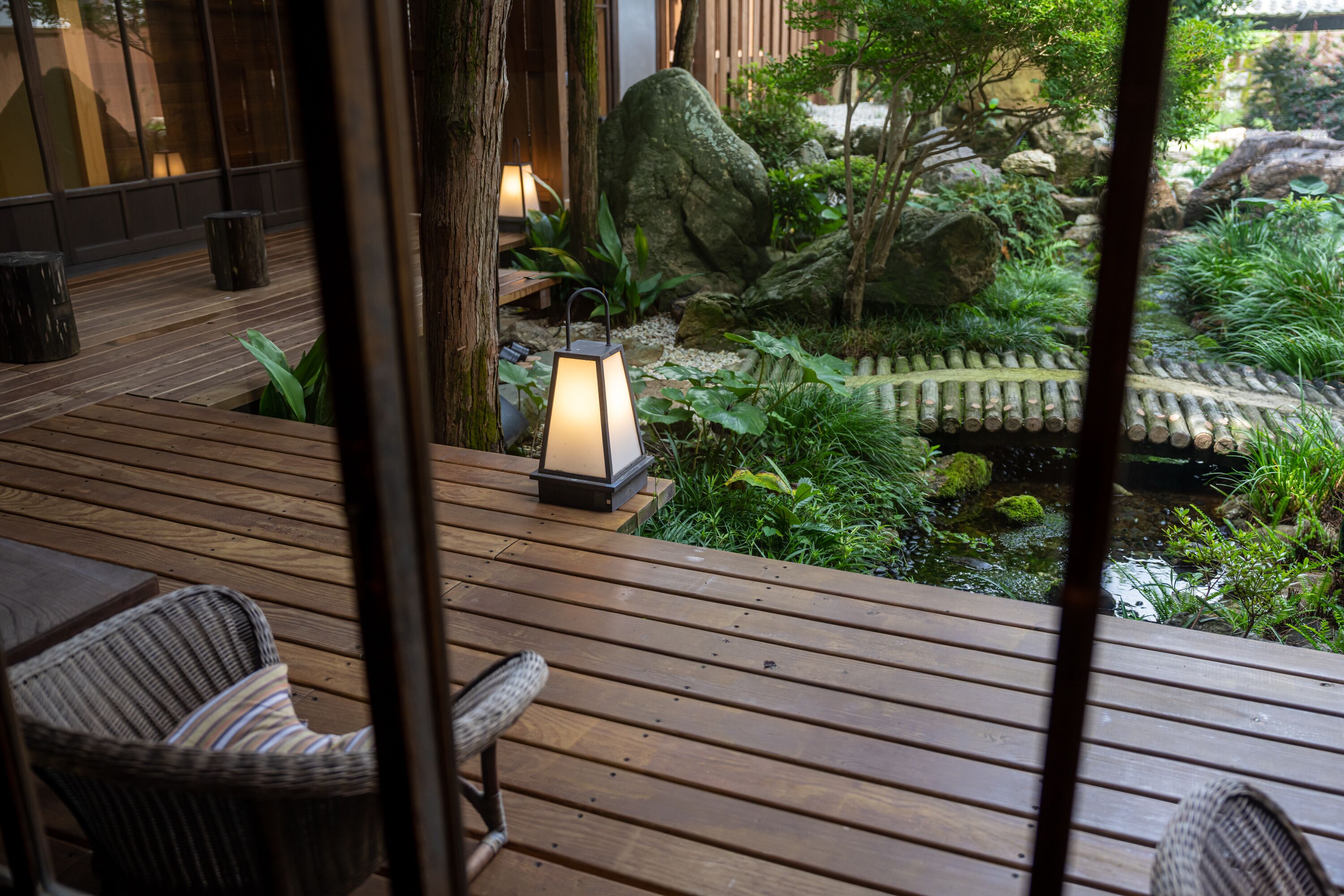 Une terrasse en bois avec des chaises, une lanterne et un jardin agrémenté de rochers et de plantes.