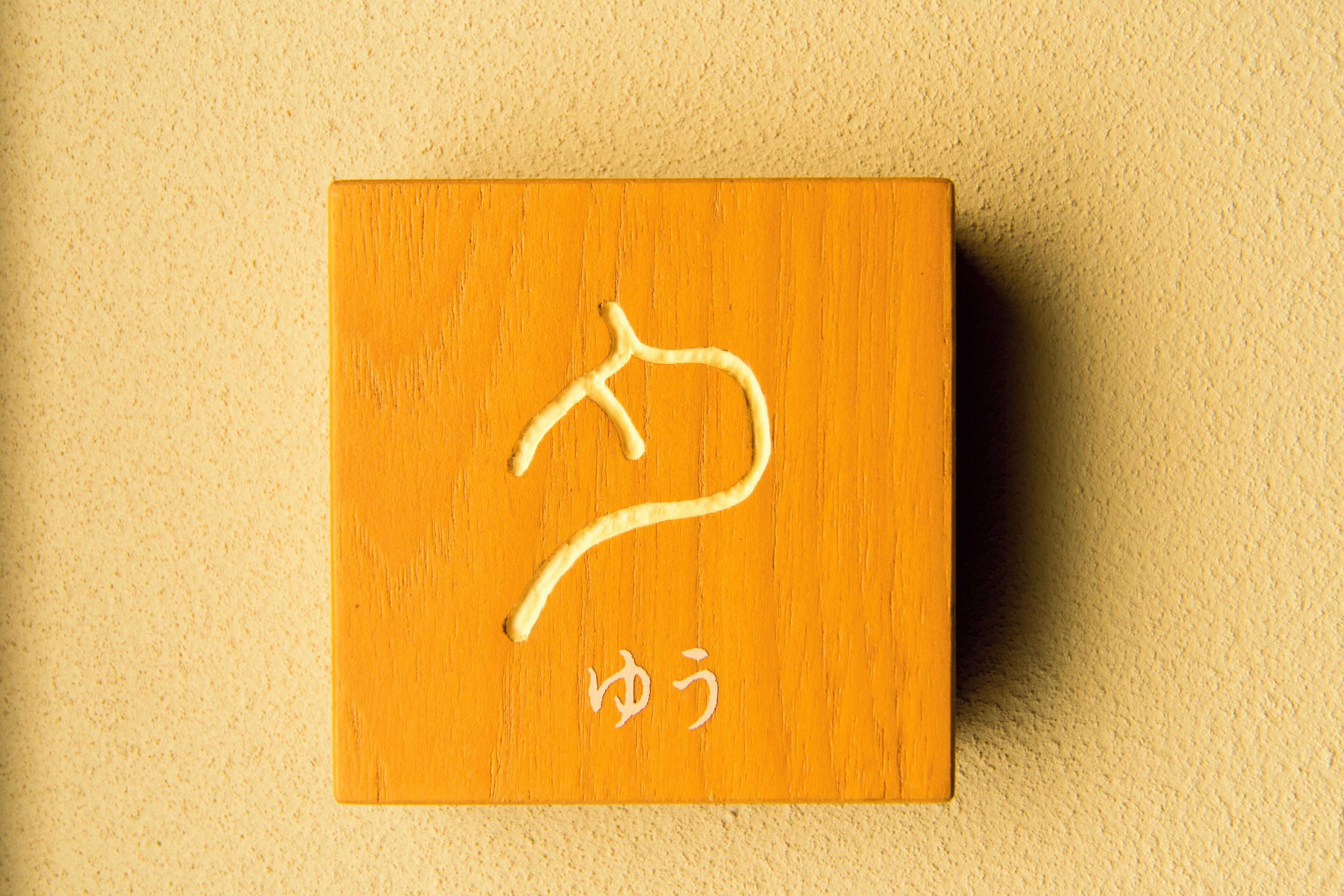 A wooden sign with a white symbol and Japanese characters.