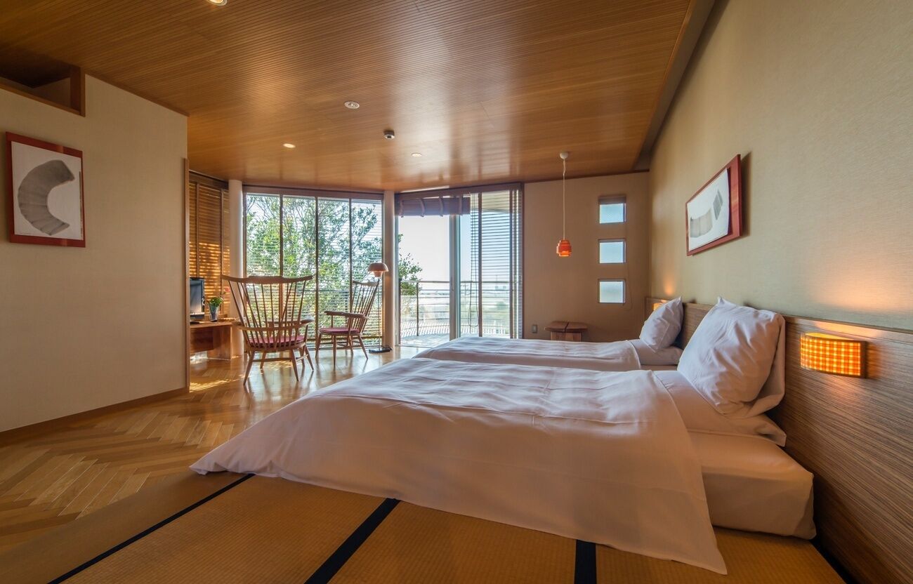 A modern hotel room with a large bed, wooden ceiling, and large windows.