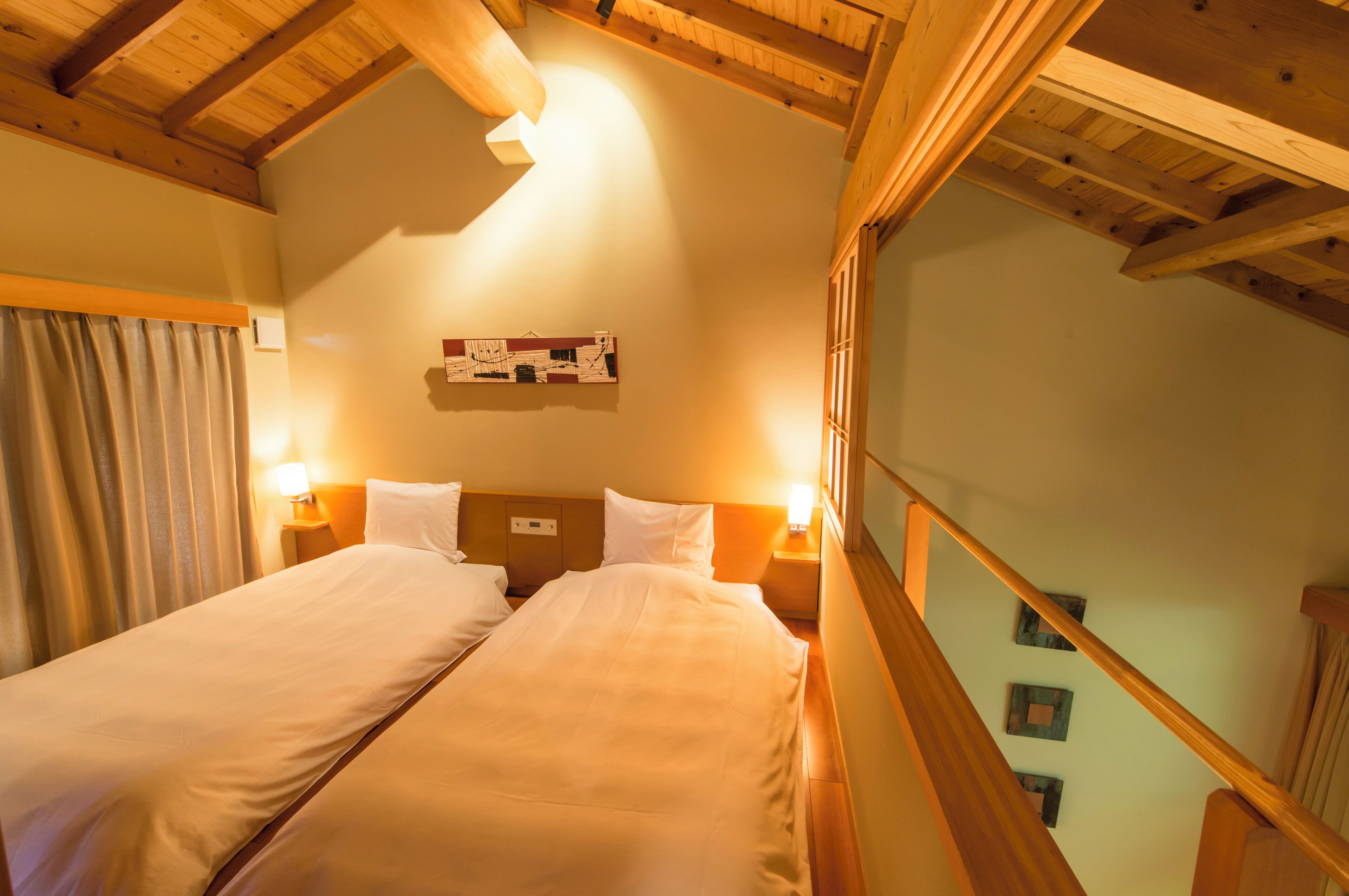 A hotel room with two beds, wooden ceiling beams, a wall-mounted artwork, and a staircase.