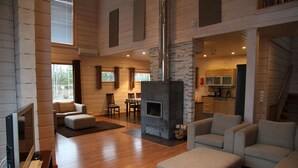 Amplia sala de estar con chimenea, pisos de madera y una cocina al fondo.