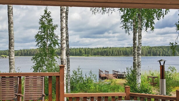 Una terraza de madera con un jacuzzi, sillas de madera y vistas a un lago rodeado de abedules.