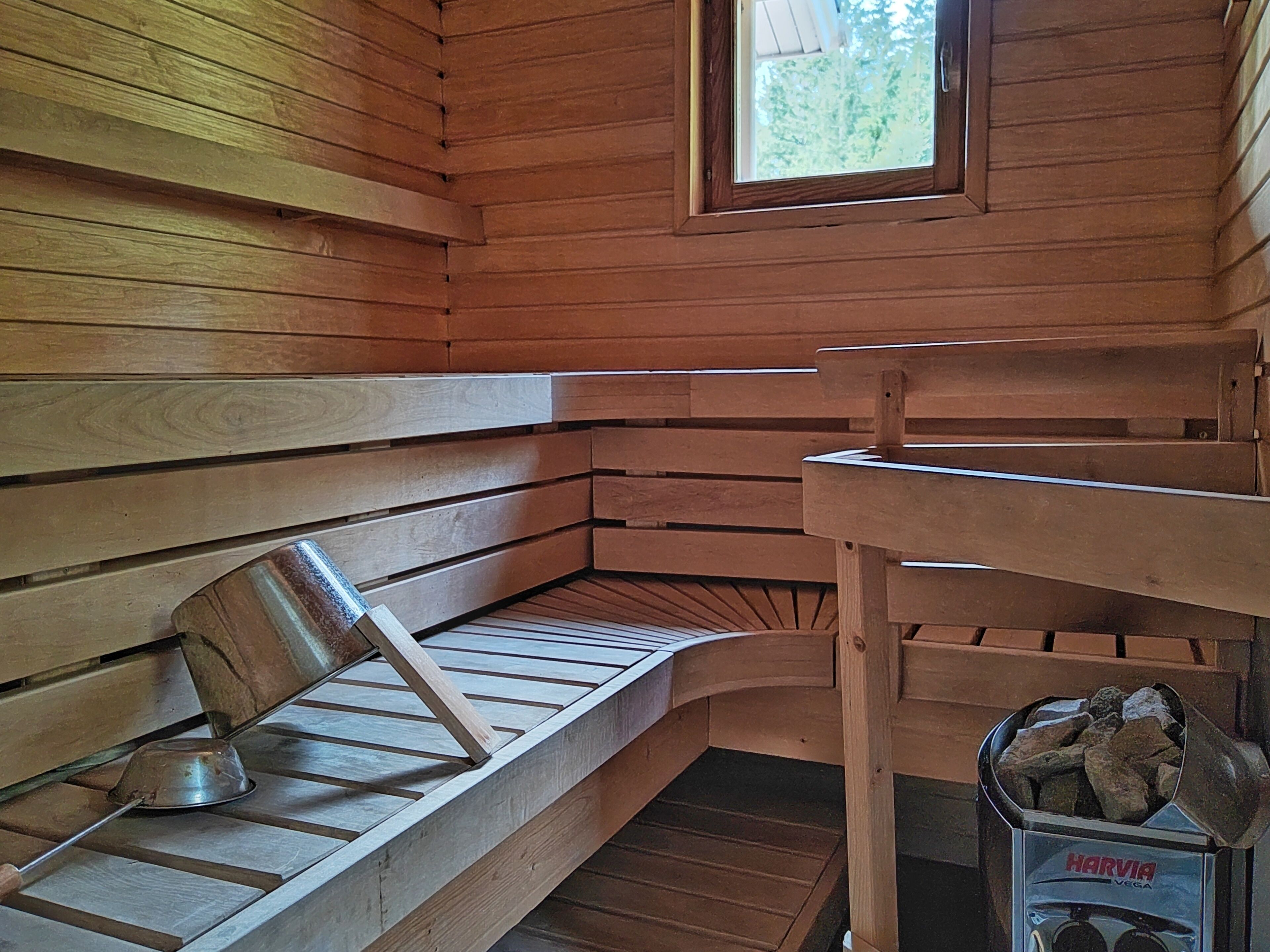 A wooden sauna with benches, a metal basin, and a container of rocks.
