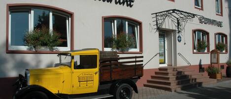 A vintage yellow truck parked in front of a cafe with a wooden bench and potted plants.