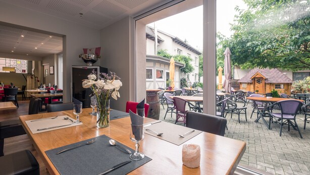 A restaurant with a wooden table set for dining, a vase of flowers, and a view of the outdoor seating area. - Notre Dame (Haguenau)