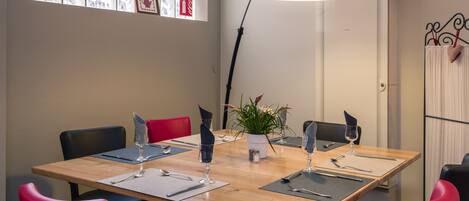 A conference room with a wooden table, red and black chairs, a potted plant, and a large floor lamp.