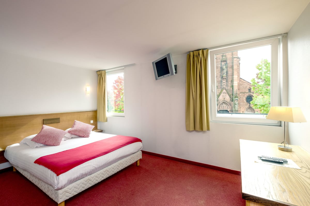 A hotel room with a bed, a desk, a TV, and a window with curtains.