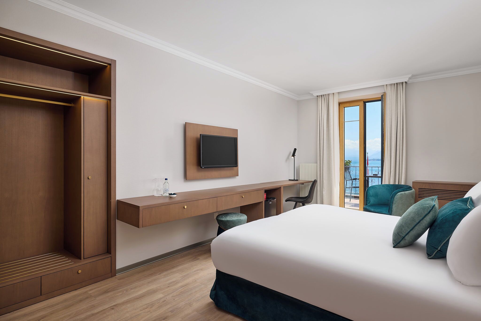 A hotel room with a large bed, a desk with a TV, a chair, and a view of the outdoors.