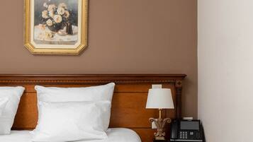 A hotel room with a large bed, a nightstand with a lamp and phone, and a framed painting on the wall.