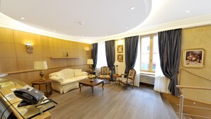 Une chambre d’hôtel avec un plancher en bois, un canapé, une table basse, un bureau avec un téléphone et une fenêtre avec des rideaux.