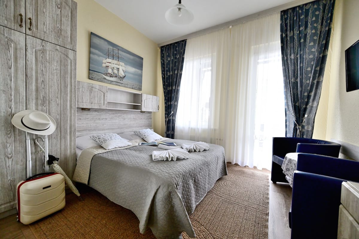 A hotel room with a bed, a suitcase, a lamp, a painting, and curtains.