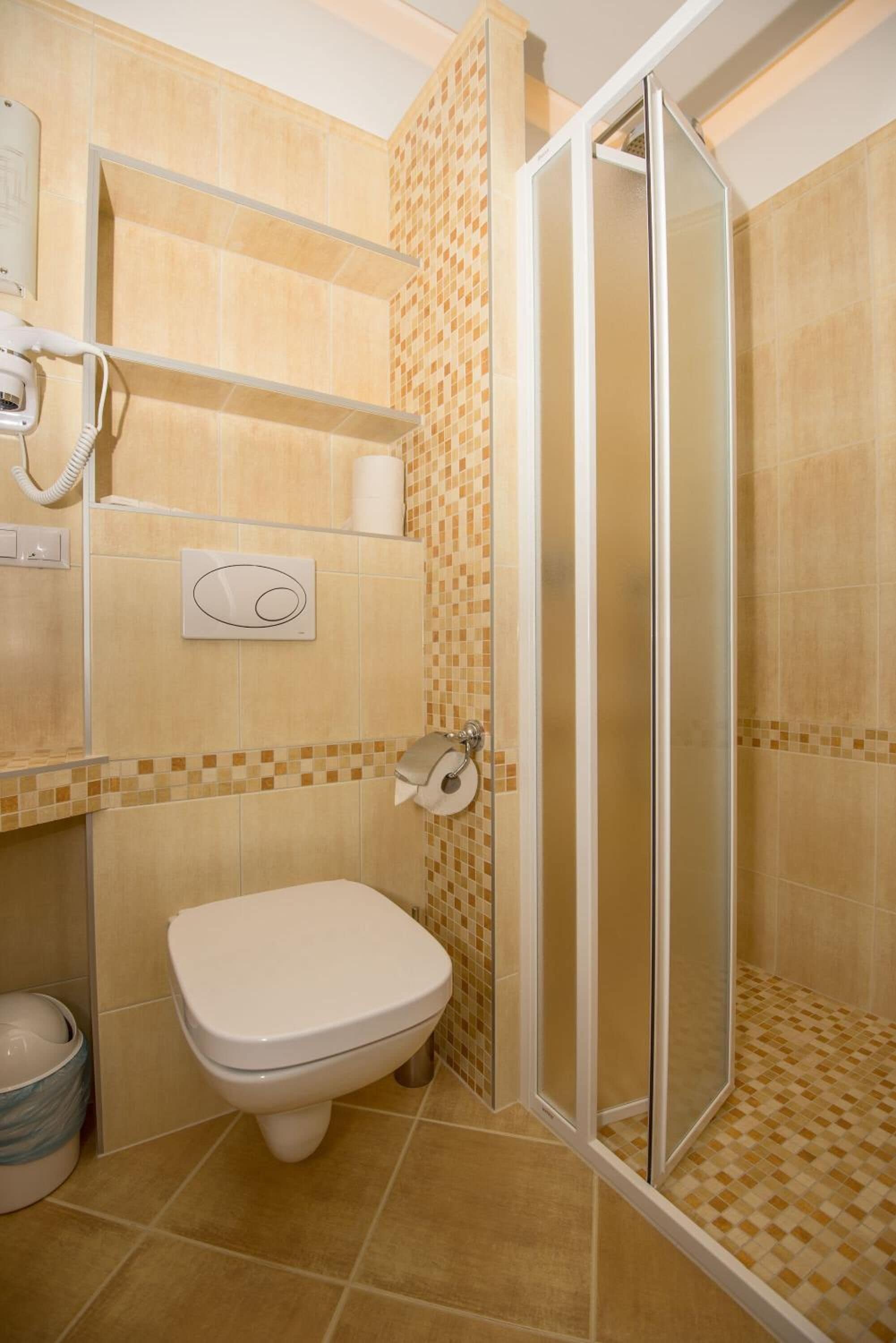 A bathroom with a toilet, a shower with a glass door, a towel dispenser, and a toilet paper holder.
