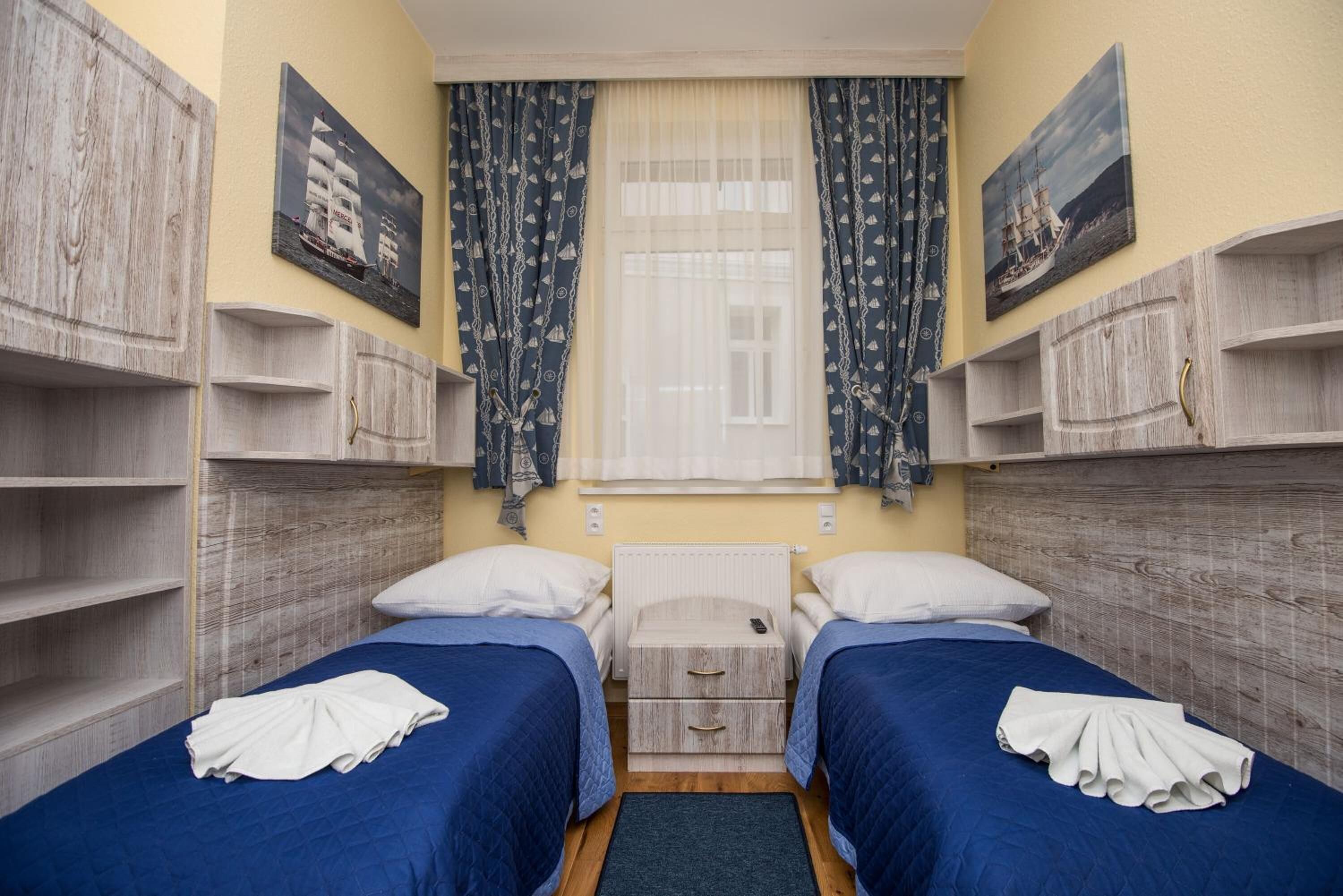 Une chambre avec deux lits, des têtes de lit en bois, une fenêtre avec des rideaux légers et des œuvres d’art accrochées au mur.