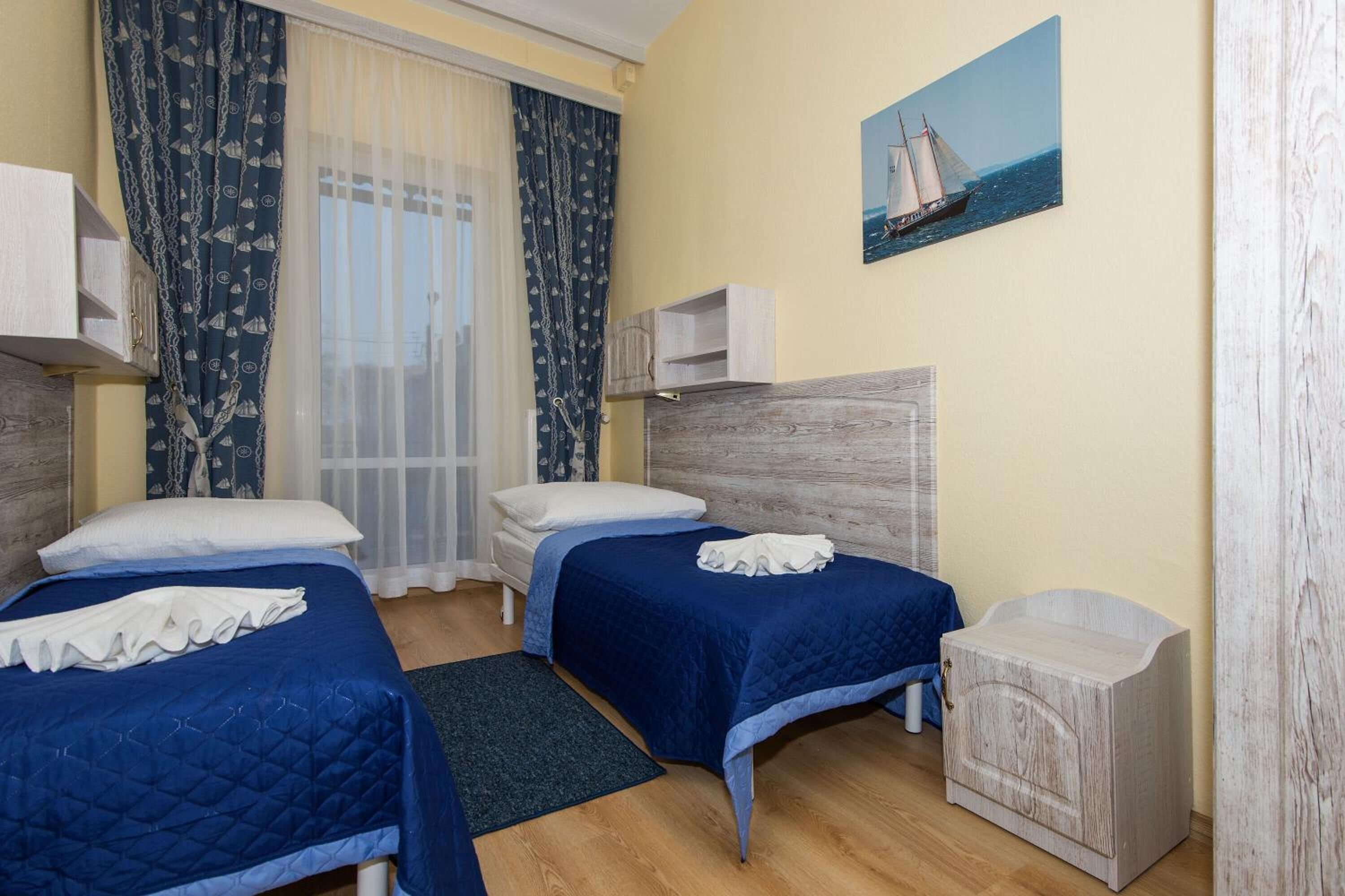 Ein Hotelzimmer mit zwei Betten, einem Holzkopfende, einem Bild eines Segelboots und einer kleinen Holzkiste.