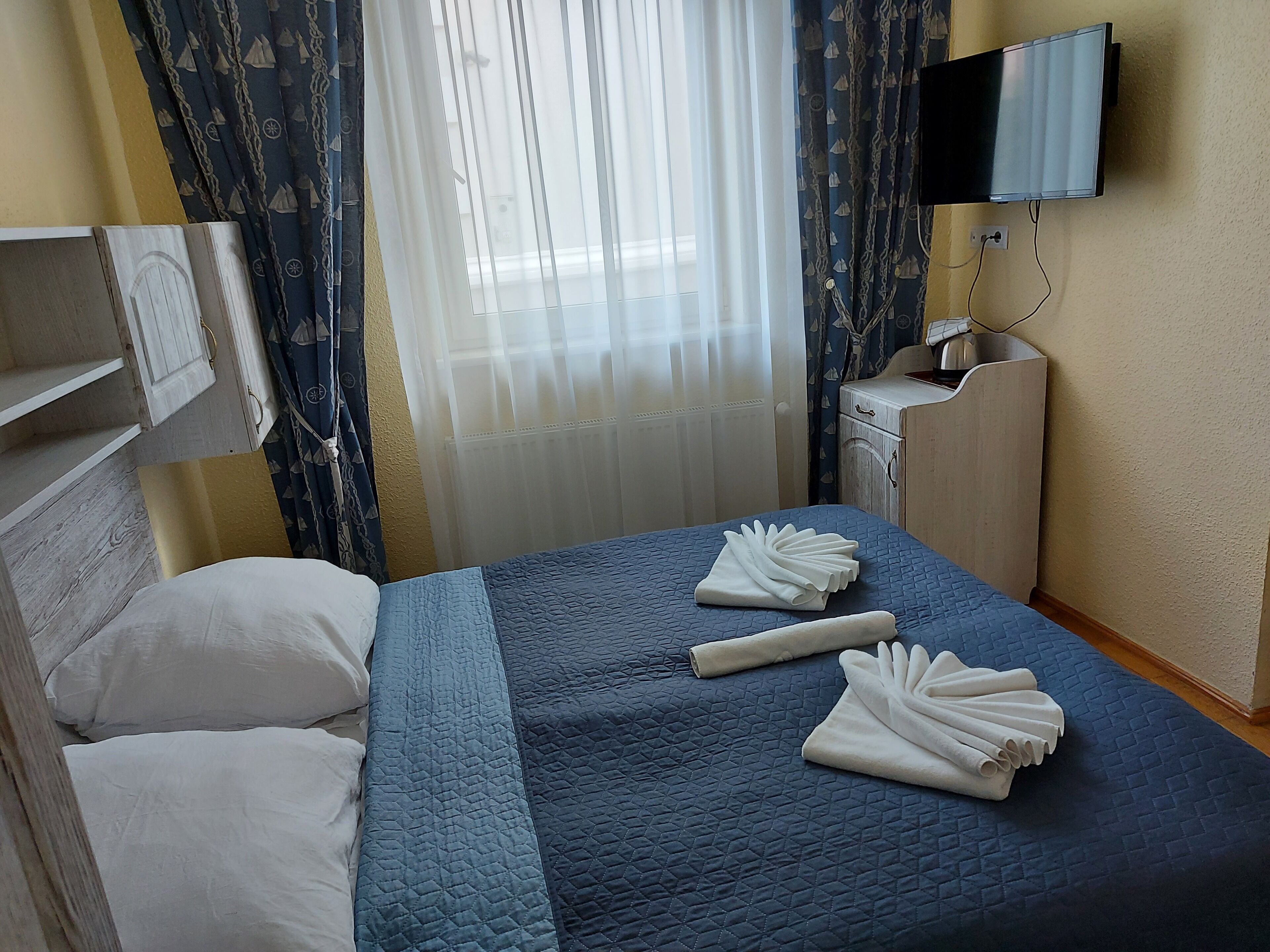 Ein Hotelzimmer mit Bett, Wandfernseher, Holzschrank und einem fenster mit Vorhängen.