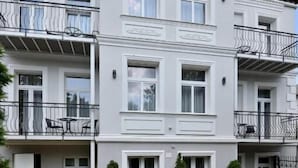 Un edificio residencial de varios pisos con balcones, mobiliario exterior y plantas en macetas.