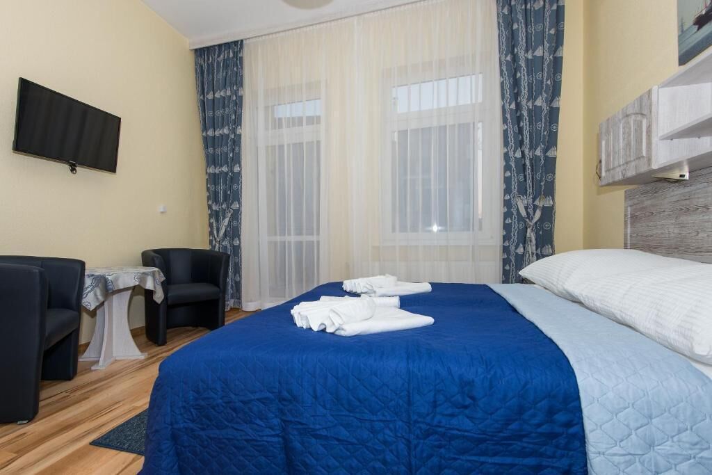 Habitación de hotel con una cama grande, dos sillones, una mesita y un televisor en la pared.