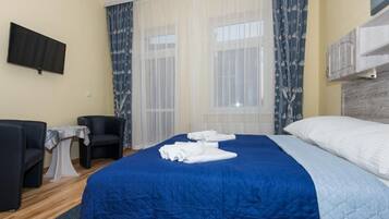 Habitación de hotel con una cama grande, dos sillones, una mesita y un televisor en la pared.