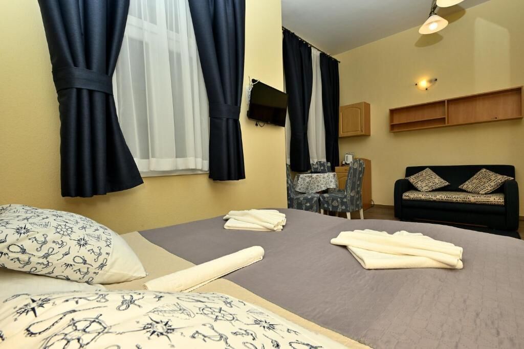 A hotel room with a bed, a desk, a chair, a sofa, and a television on the wall.