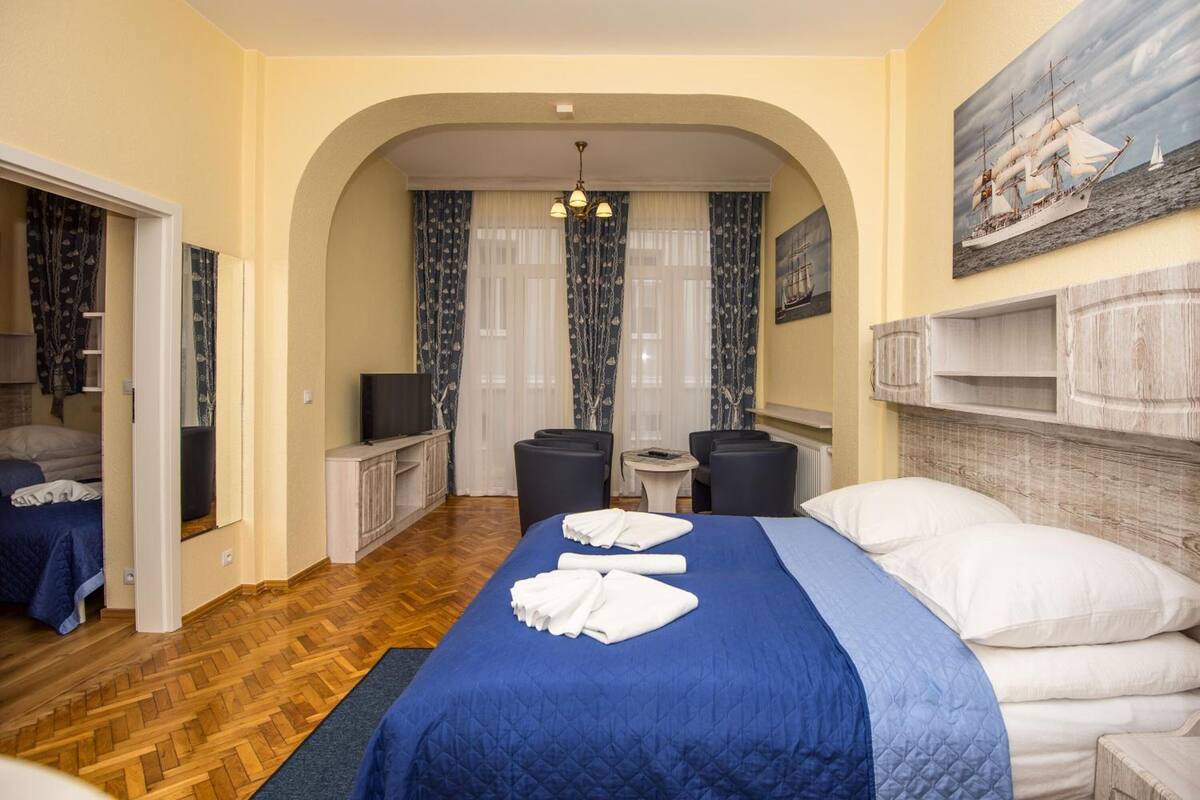 A hotel room with a large bed, a desk, a chair, and a small table. There is a painting on the wall and a window with curtains.
