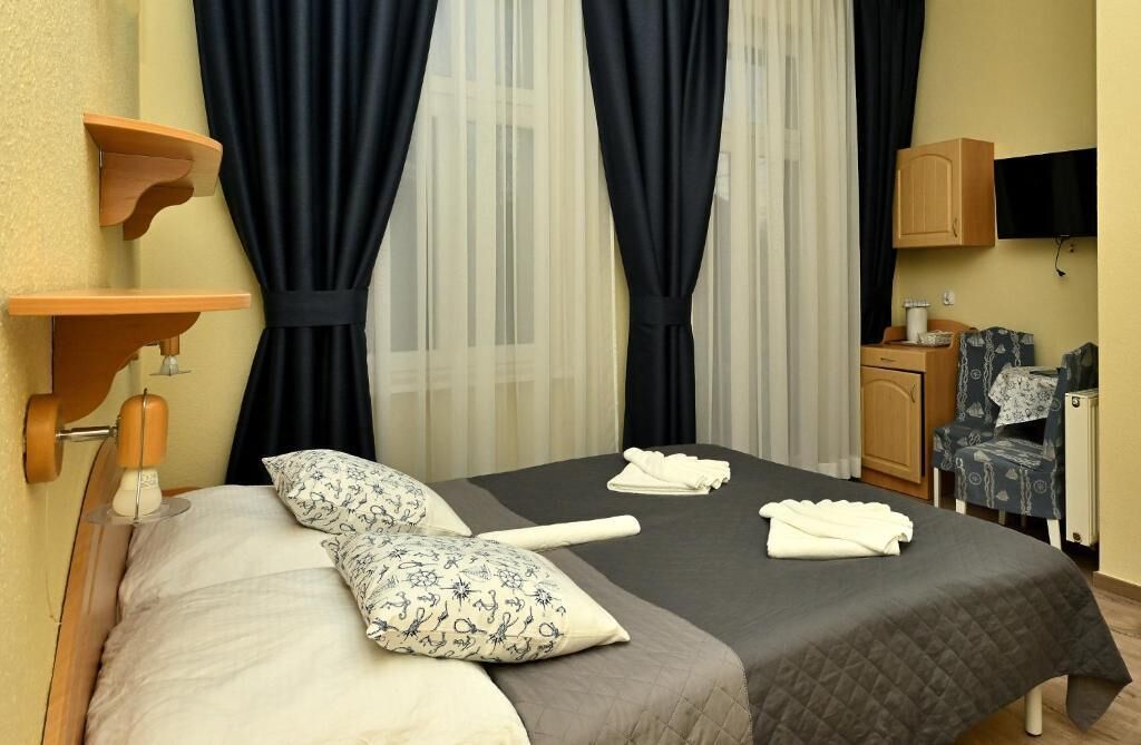 Ein Hotelzimmer mit einem Bett, zwei Kissen, einem Nachttisch mit Lampe, einem Sessel, einem Fernseher und einem Schrank.