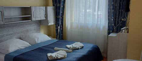 A hotel room with a bed, a desk, a chair, and a window with curtains.
