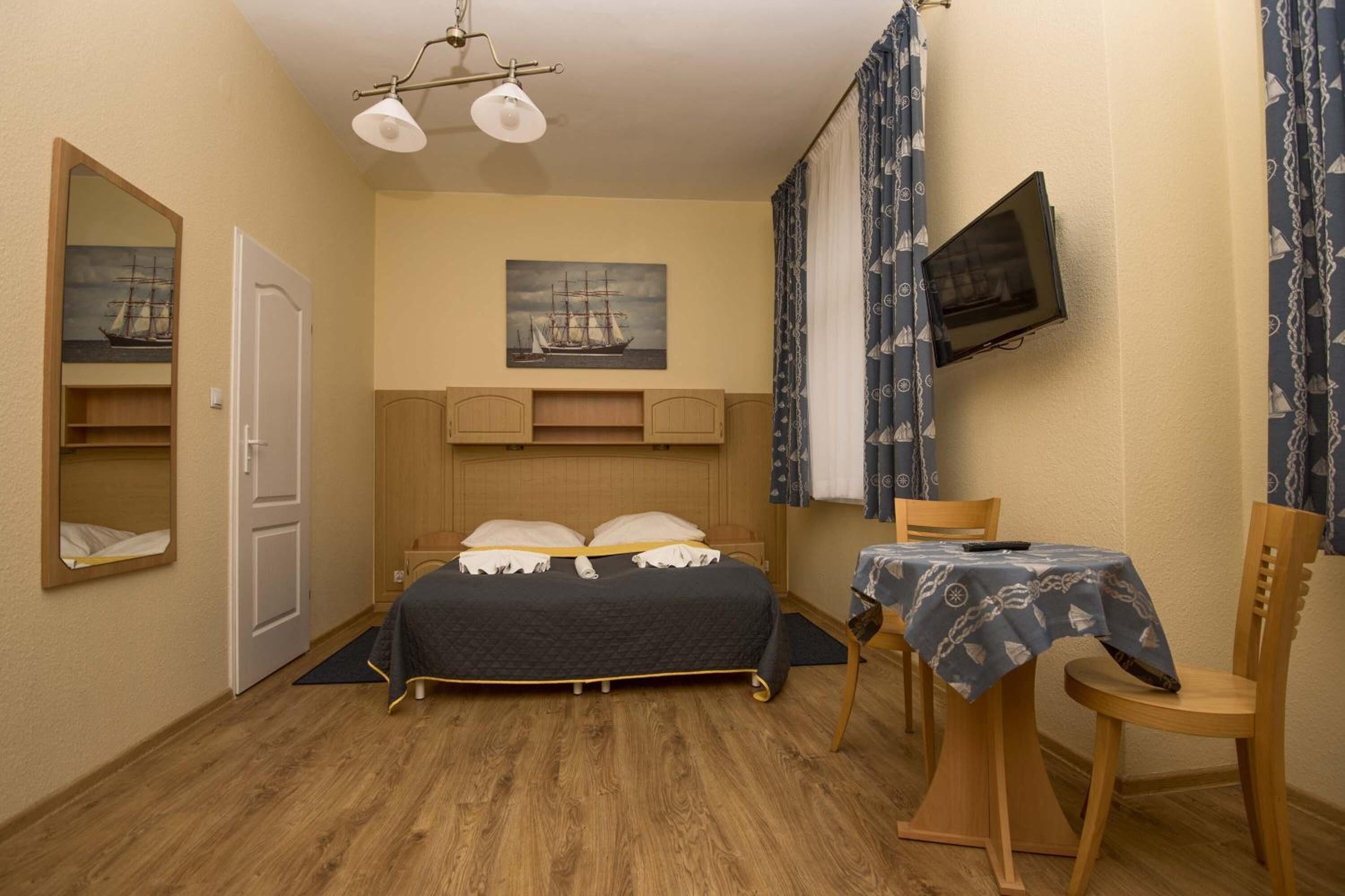 Ein Schlafzimmer mit einem Bett, einem an der Wand befestigten Fernseher, einem kleinen Tisch mit Stuhl und einer Tür.