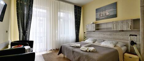 A neatly arranged hotel room with a bed, a desk, a chair, a dining table with a fruit bowl, and a large window with curtains.