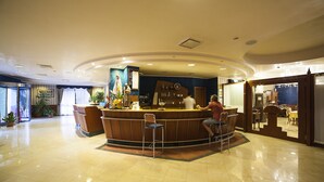 A hotel lobby with a reception desk, chairs, potted plants, and a large painting on the wall. - Hotel Villa San Pietro (San Giovanni Rotondo)