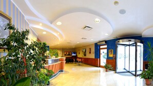 A hotel lobby with a reception desk, seating area, and a large window. - Hotel Villa San Pietro (San Giovanni Rotondo)