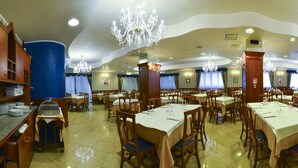 A spacious dining area with multiple tables and chairs, a chandelier, and a blue accent wall. - Hotel Villa San Pietro (San Giovanni Rotondo)