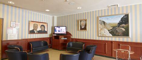 A lobby with striped walls, a television, framed portraits, and seating areas.